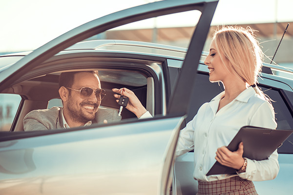 Happy sales woman giving car keys to customer